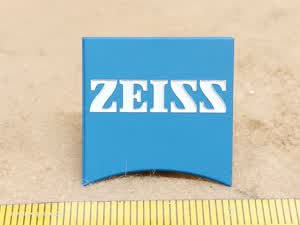 Zeiss Axiovert 100M plakietka mikroskopowa z łukiem soczewki i logo producenta w zaokrąglonych literach